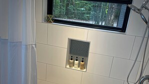A modern bathroom with a built-in window, a shower, and a vanity with a tray holding toiletries. - **Cleaning Fee Included** Mini modern cabin nestled in the peaceful hills between Jackson and Putnam County, minutes away from CUMMINS FALLS STATE PARK. Designed for comfort and style, this vacation rental seamlessly blends modern charm with wooded s (Cookeville)
