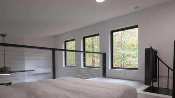 A modern bedroom with a bed, large windows, a staircase, and a pendant light. - **Cleaning Fee Included** Mini modern cabin nestled in the peaceful hills between Jackson and Putnam County, minutes away from CUMMINS FALLS STATE PARK. Designed for comfort and style, this vacation rental seamlessly blends modern charm with wooded s (Cookeville)