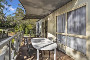 A covered outdoor patio with a table and chairs, large windows, and a view of the surrounding trees. - 2 Bedroom Luxury Villa (Metung)