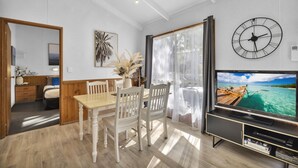 A modern living room with a wooden dining table, white chairs, a large TV, and a wall clock.