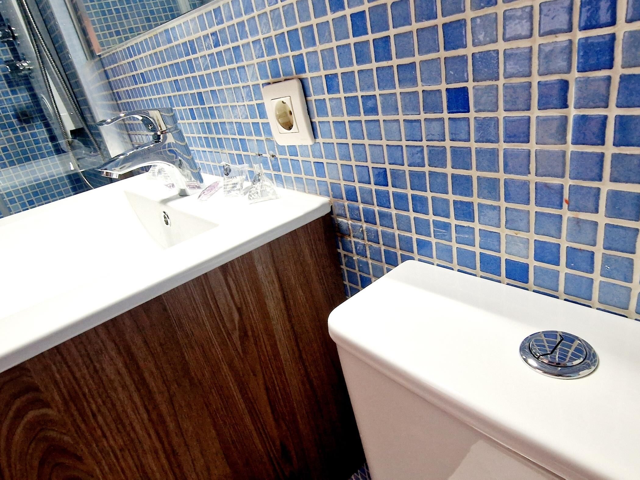 Ein Badezimmer mit einem weißen Waschbecken, einem Spiegel und einer Toilette mit blauen Mosaikfliesen.