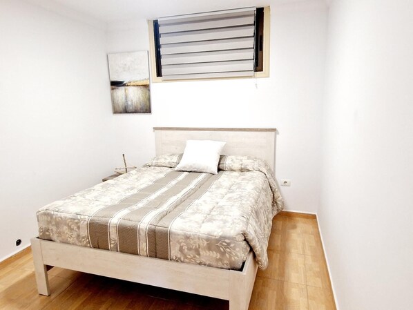 A bedroom with a bed, a headboard, a nightstand, a wall-mounted artwork, and a window with blinds.