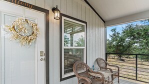 A porch with wicker chairs, a glass door with a wreath, and a view of trees. - Hidden Fox Escape - Grey Fox (Hays County)