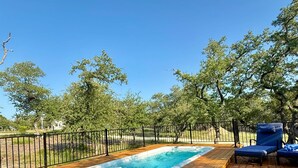 A wooden deck with a hot tub, surrounded by a black metal fence, and trees in the background.