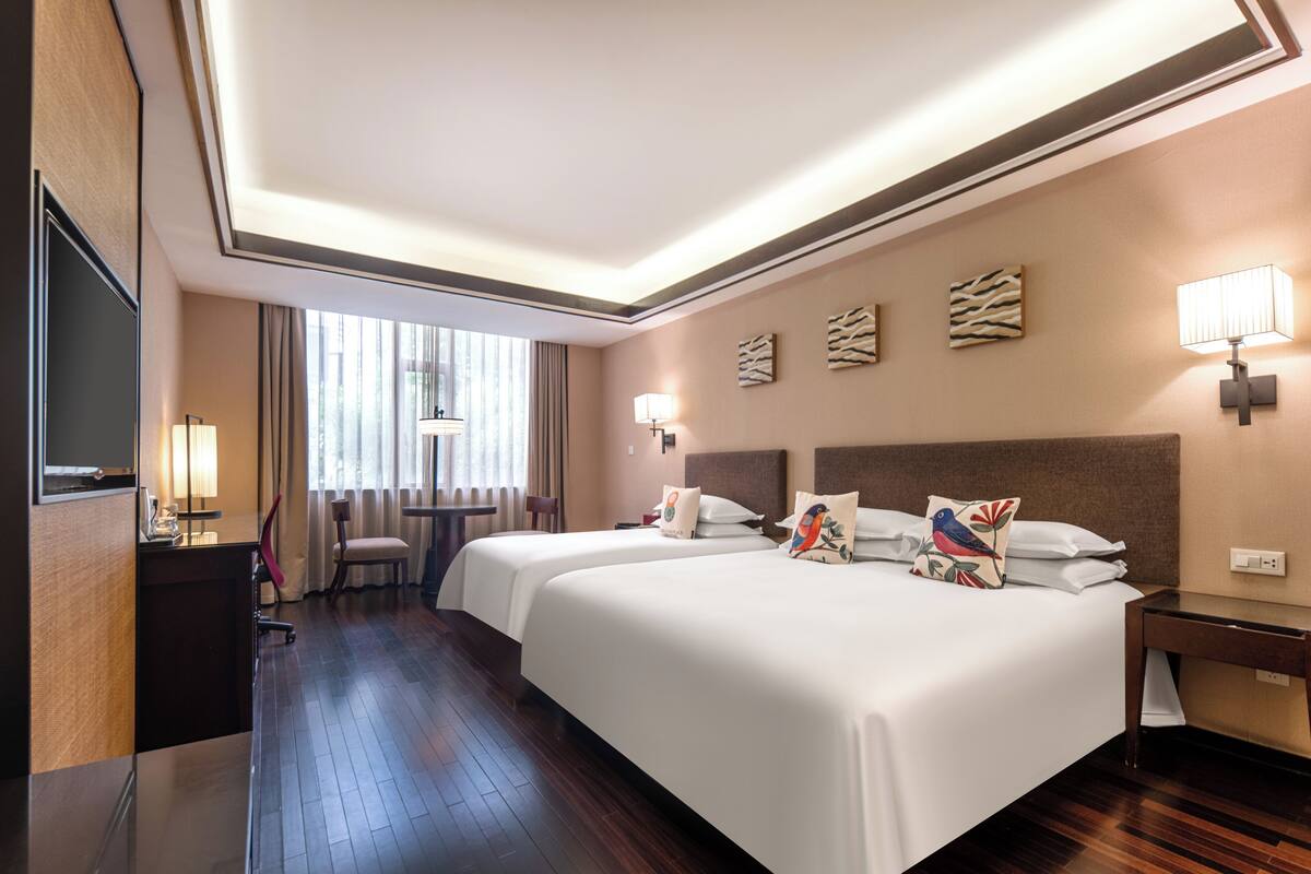 Ein Hotelzimmer mit zwei Betten, einem Schreibtisch, einem Stuhl, einem Fernseher und einem Fenster mit Vorhängen.