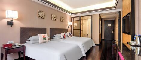 Ein Hotelzimmer mit zwei Betten, einem Nachttisch, einem Schreibtisch, einem Spiegel und einem durchgegangenen Türrahmen einsehbarer Badezimmers.