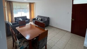A living room with a dining table, two sofas, and a door. - 🏡 Cozy Apartment in Piura - Safe, Central and Comfortable (Piura)