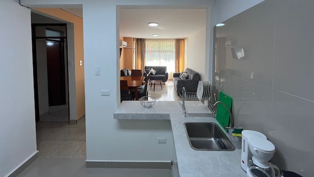 A modern kitchen with a built-in sink, a dining area with a table and chairs, and a living room with a sofa and a TV. - 🏡 Cozy Apartment in Piura - Safe, Central and Comfortable (Piura)