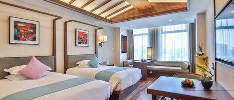 A hotel room with two beds, a dining table, a potted plant, and artwork on the walls.