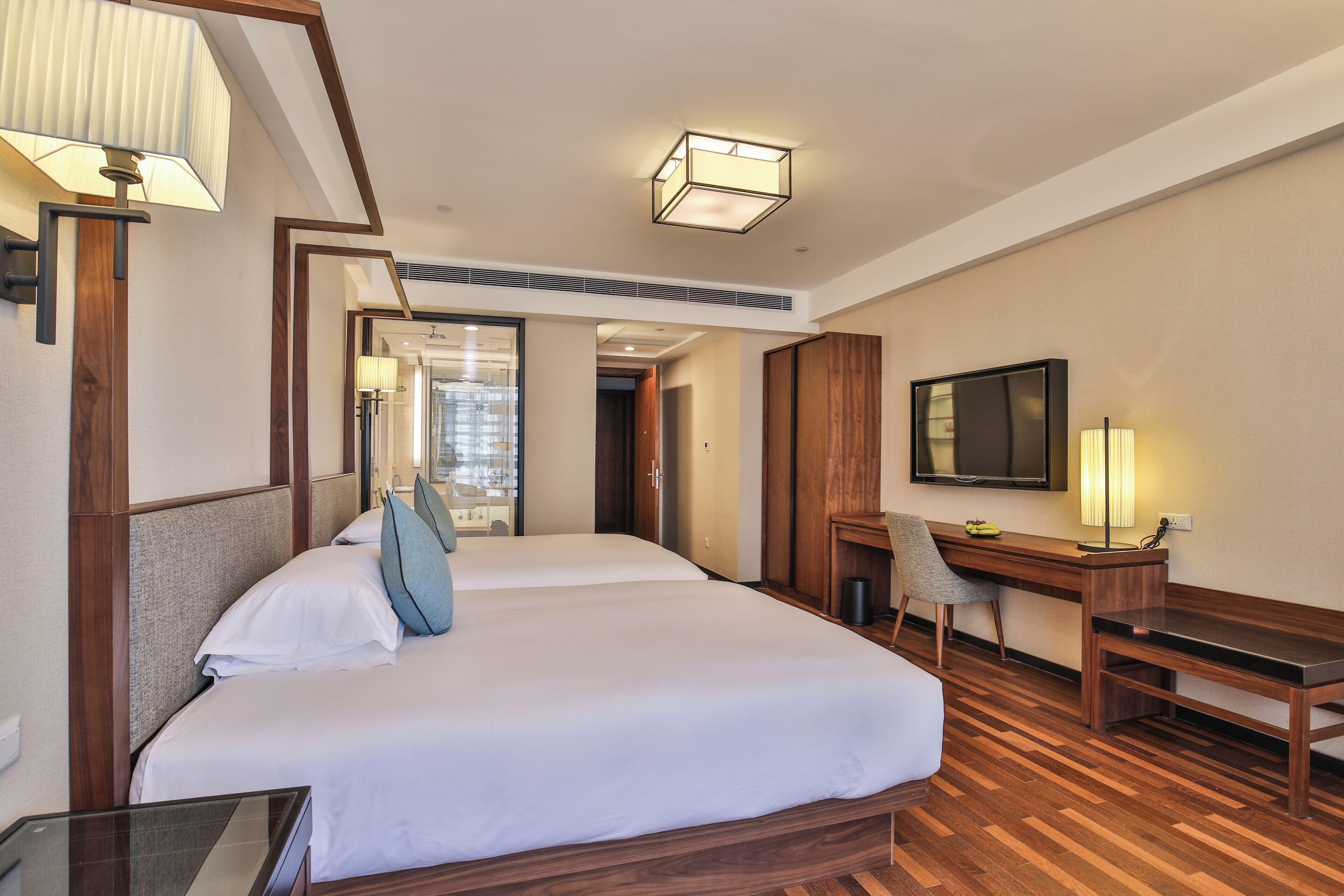 A hotel room with a large bed, a desk, a chair, a TV, and a lamp.