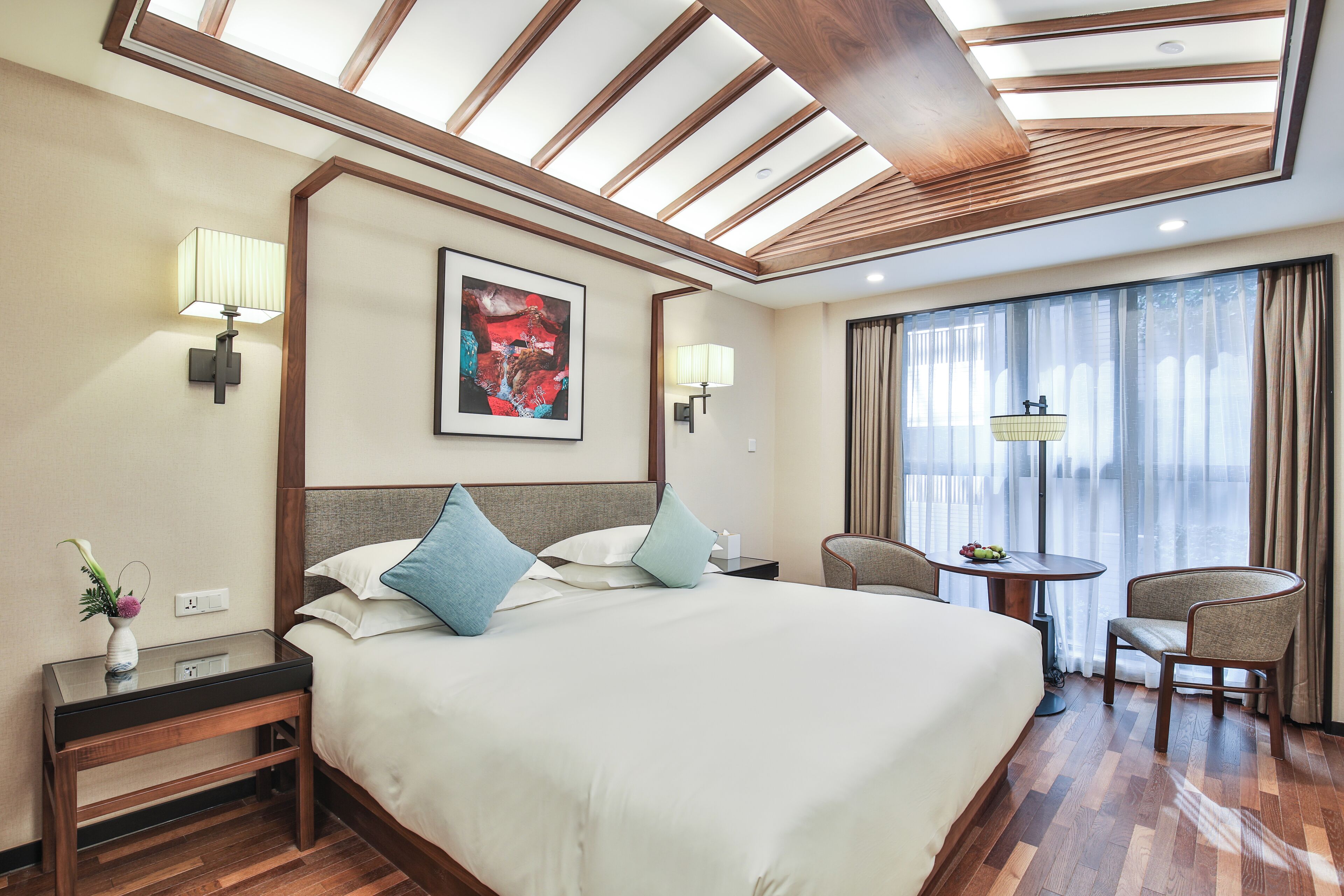 A hotel room with a large bed, two bedside tables, a desk with a chair, a window with curtains, and a skylight.