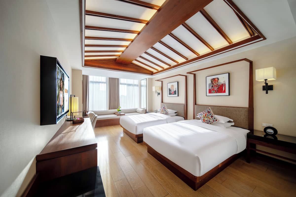 Une chambre d’hôtel avec trois lits, un bureau en bois, un téléviseur à écran plat et des œuvres d’art accrochées aux murs.