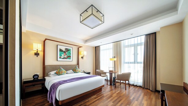 Une chambre d’hôtel avec un grand lit, des tables de chevet, un bureau, une chaise et une fenêtre avec des rideaux.
