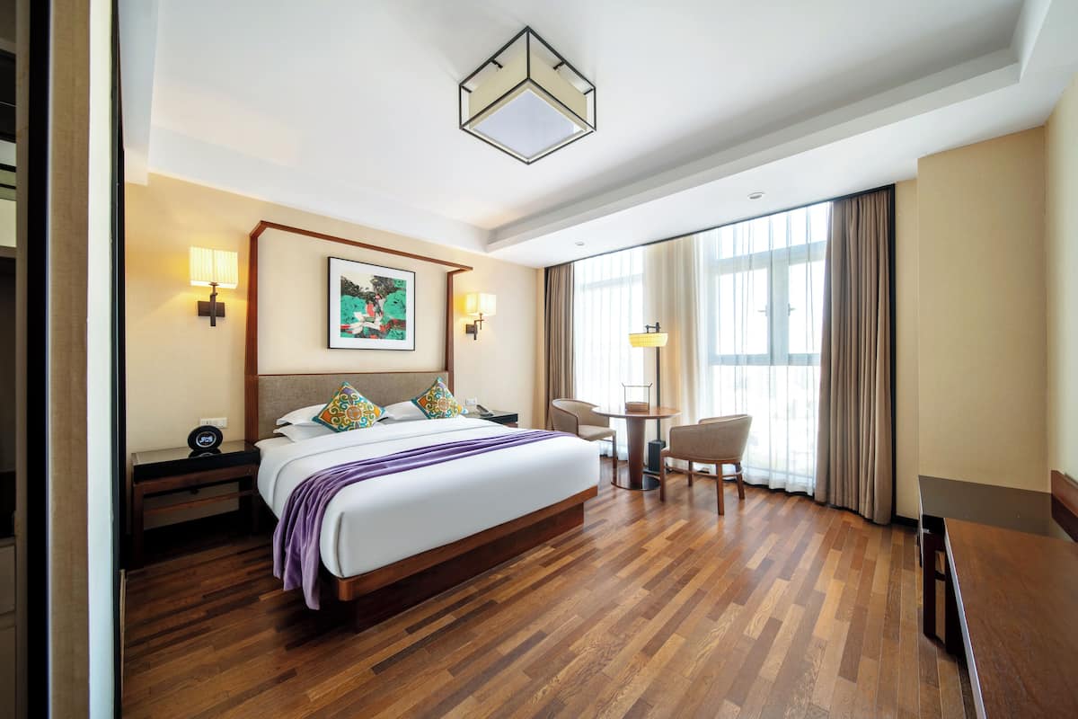 Une chambre d’hôtel avec un grand lit, des tables de chevet, un bureau, une chaise et une fenêtre avec des rideaux.