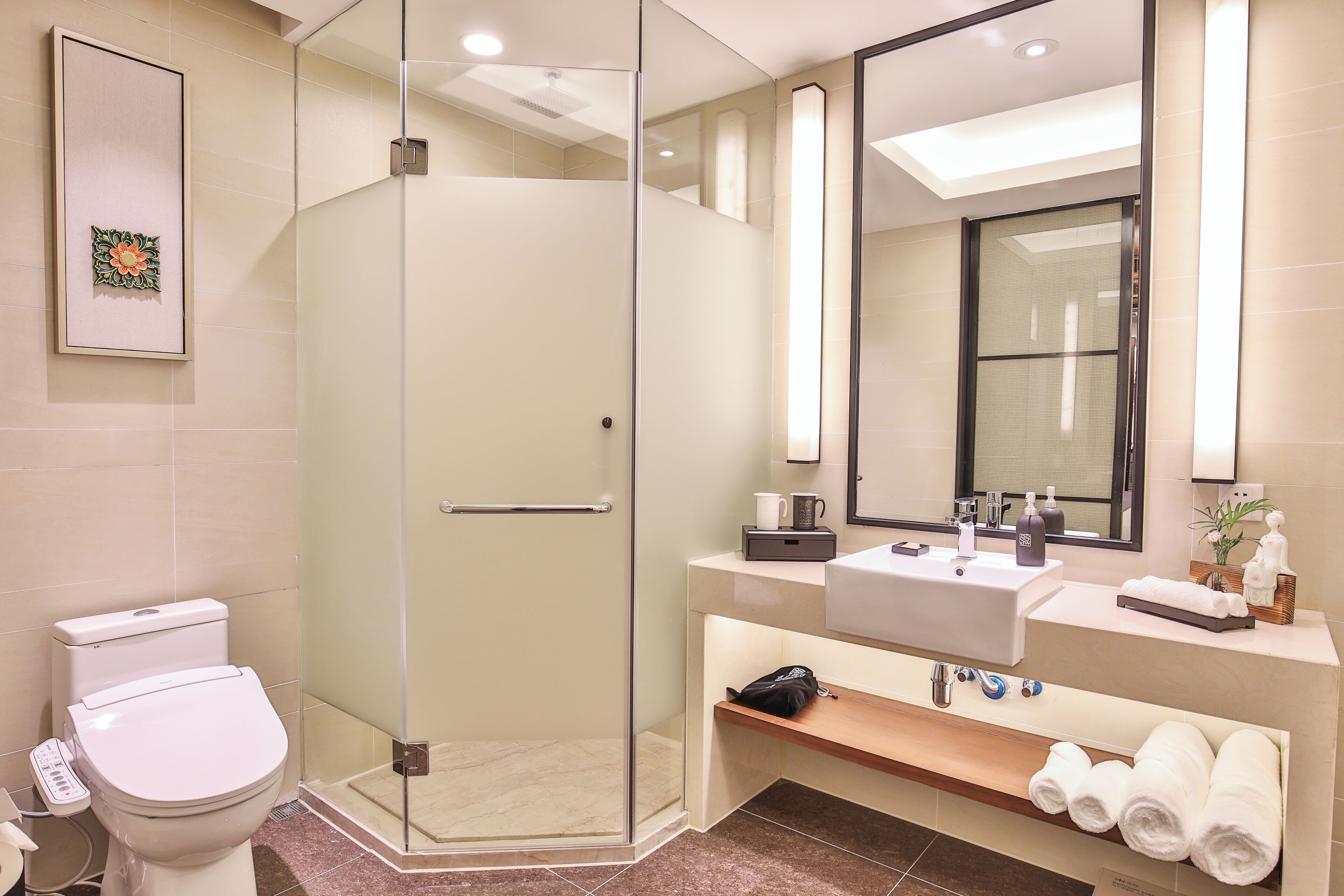 A modern bathroom with a glass-enclosed shower, a toilet, a sink with a mirror above, and a shelf with towels.