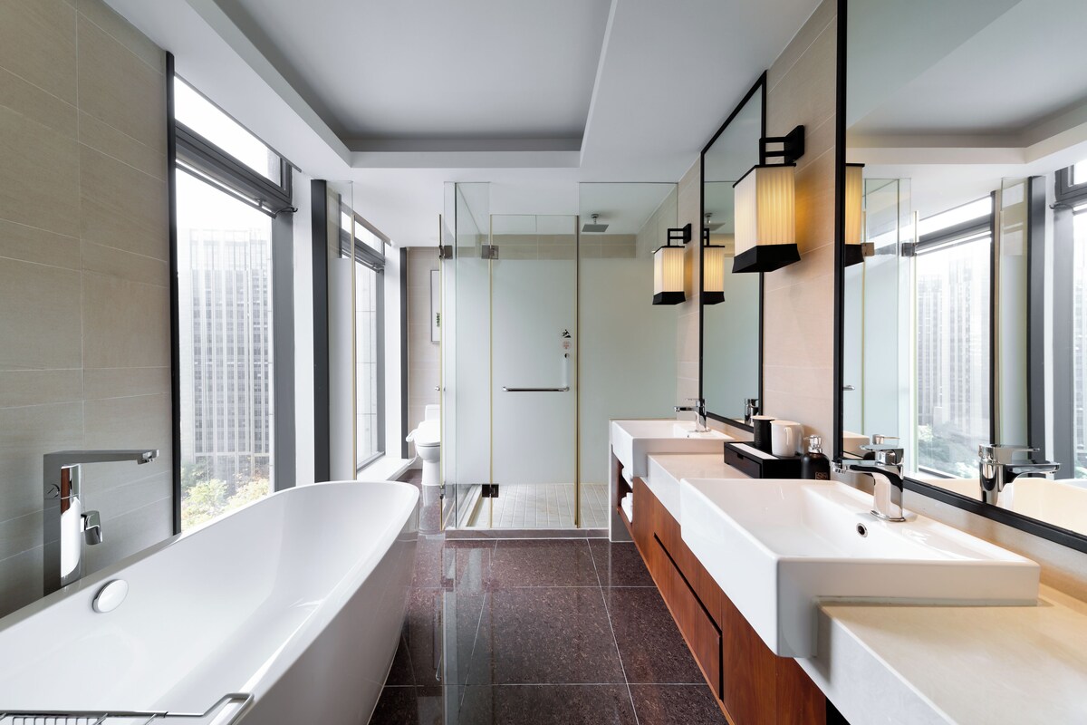 Une salle de bain moderne dotée d’une grande baignoire, de deux lavabos et d’une douche à parois de verre.