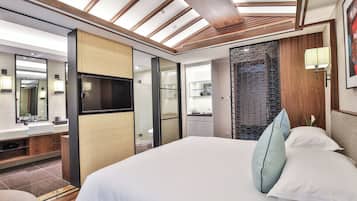 A modern hotel room with a large bed, a flat-screen TV, a bathroom with a mirror and sink, and a wooden ceiling.