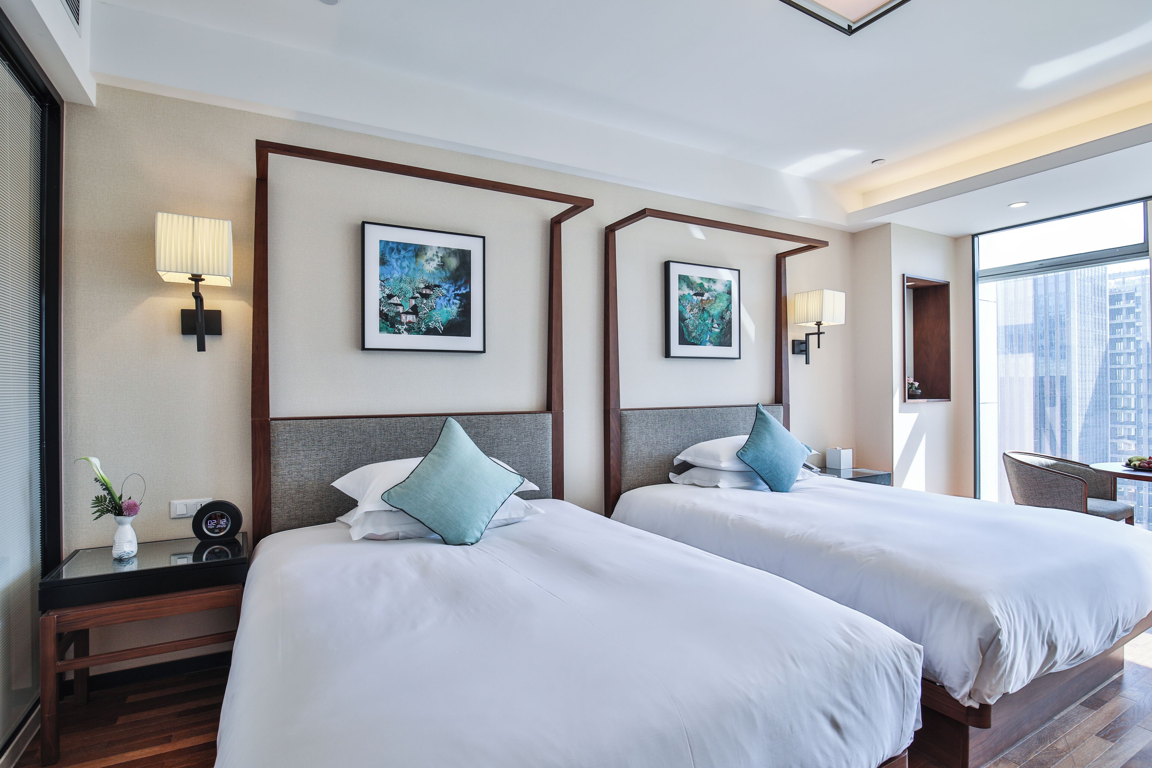 A hotel room with two beds, a nightstand, a lamp, and framed artwork on the wall.