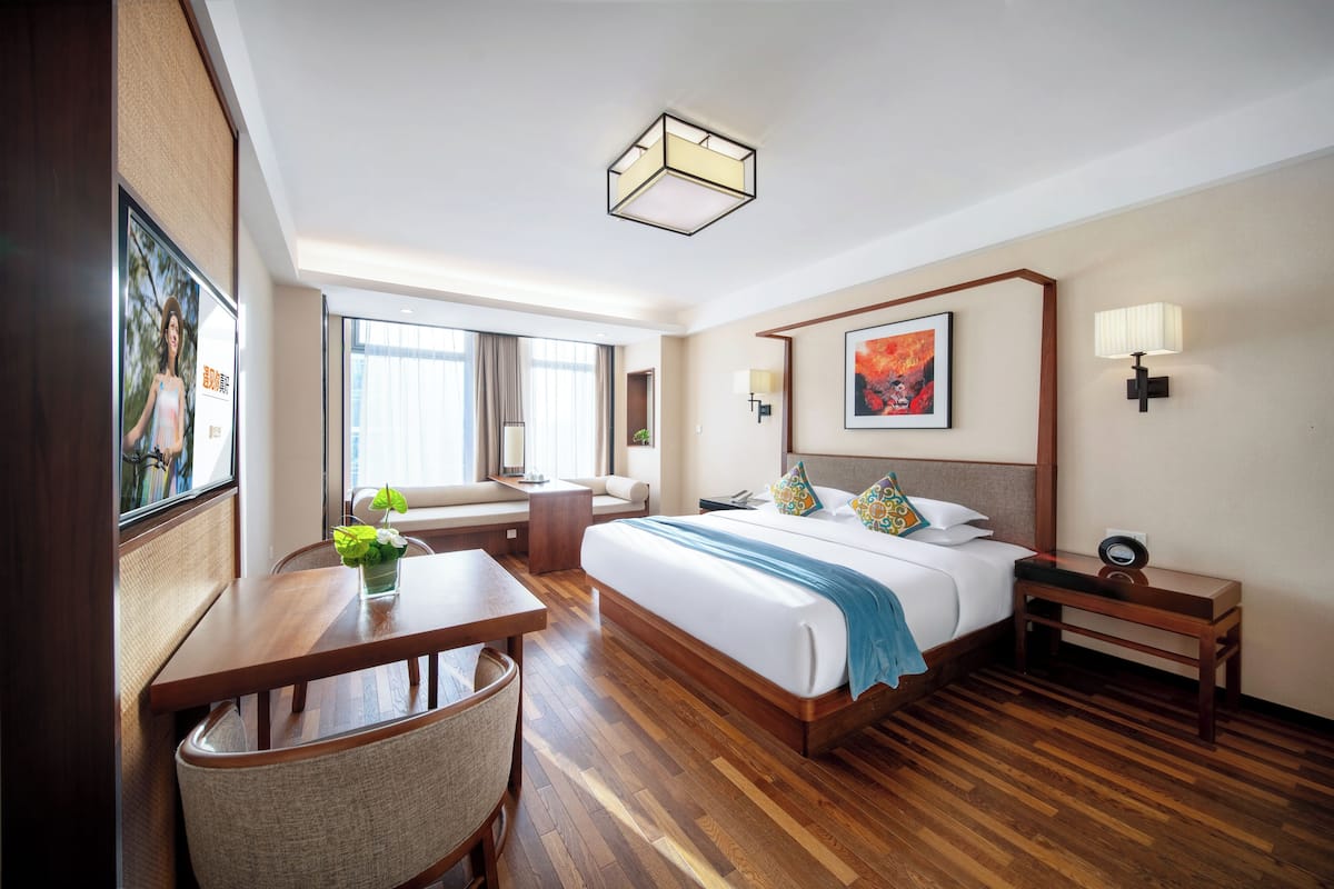Une chambre d’hôtel avec un grand lit, un bureau, une chaise, une table de chevet et une fenêtre avec des rideaux.
