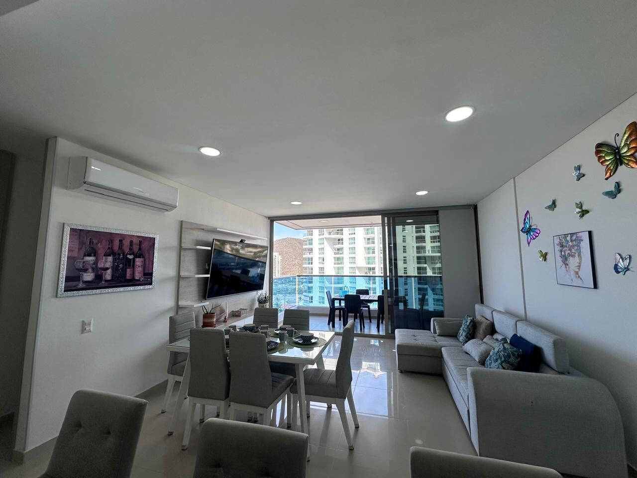 A modern living room with a dining area, a flat-screen TV, and a balcony with a city view.