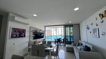 A modern living room with a dining area, a flat-screen TV, and a balcony with a city view.