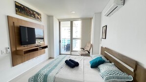 Une chambre avec un lit, un téléviseur fixé au mur, une chaise et une vue sur le balcon extérieur.
