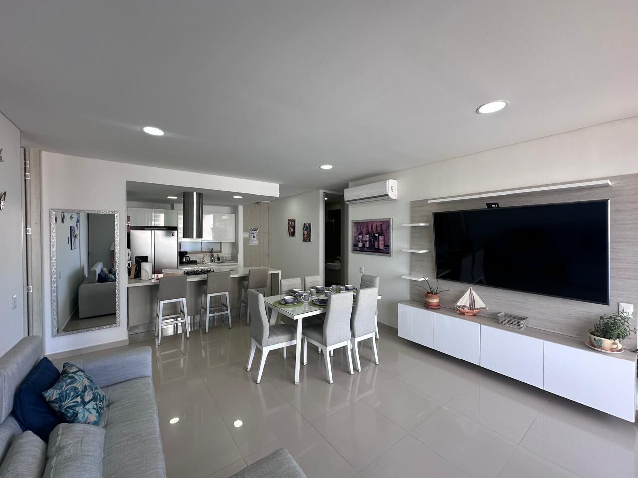 Una sala moderna con comedor, cocina y un televisor grande montado en la pared.