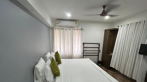 Une chambre d’hôtel équipée d’un lit, d’un ventilateur de plafond, d’un appareil de climatisation, d’une fenêtre avec des rideaux et d’une armoire en bois.