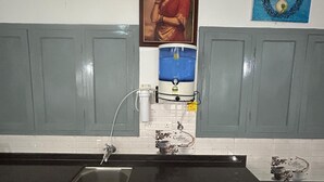 Une cuisine équipée d’un évier, d’un distributeur d’eau et d’une machine à café. Un tableau encadré est accroché au mur, et un objet décoratif est placé au-dessus de l’évier.