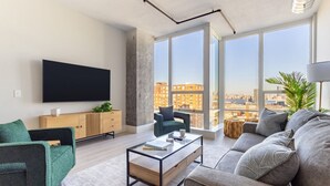 A modern living room with a large flat-screen TV, a wooden cabinet, and a sofa. - Chique Loft 10 Min from NYC with Gym, Pool, Sauna (Jersey City)