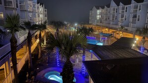 A hotel courtyard with multiple swimming pools, palm trees, and a well-lit walkway. - Seascape 2202 The Seashell Pearl Beachfront Condo Gulf View Pool Hottubs Netflix (Galveston)