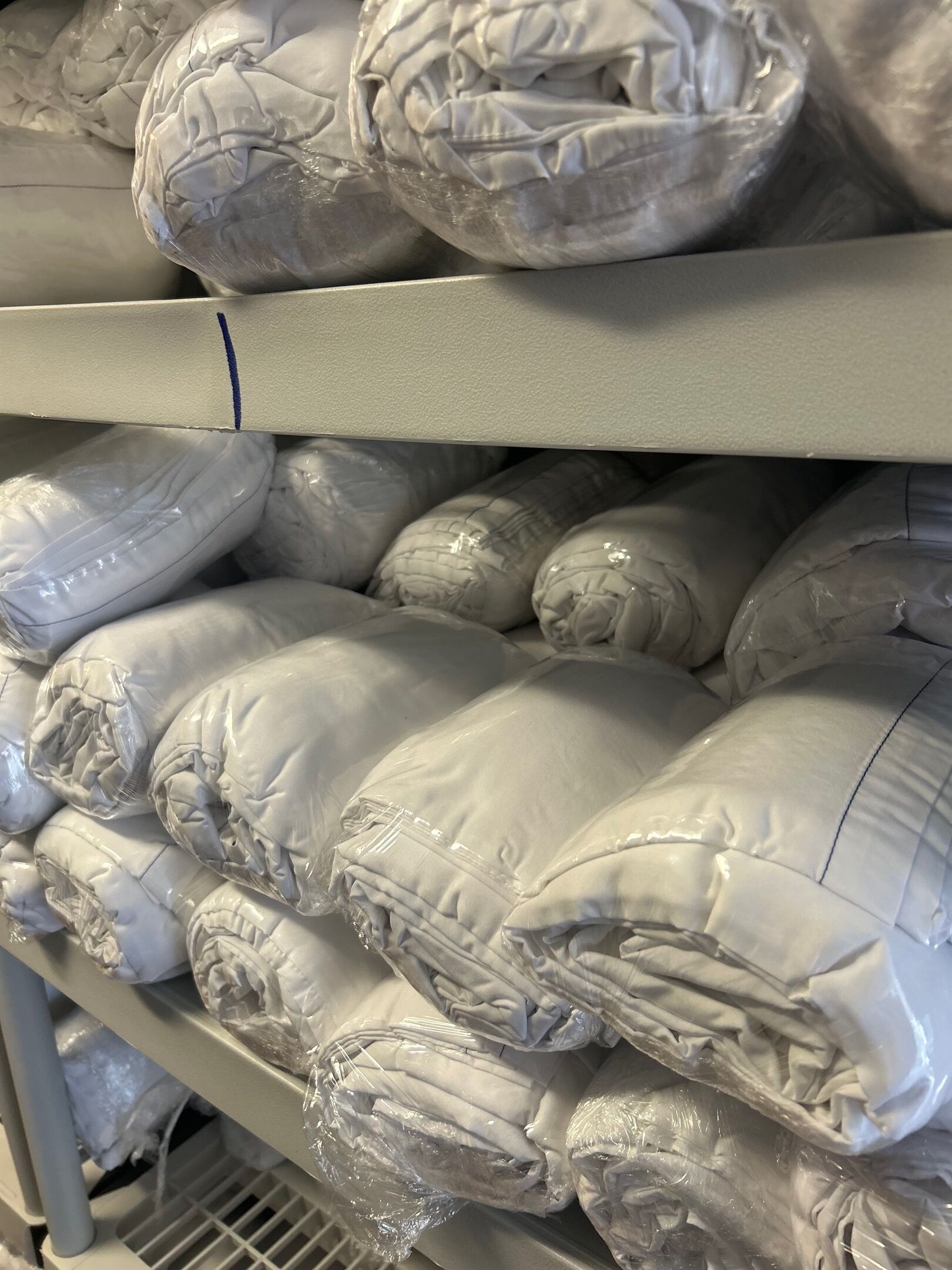 Shelves with neatly stacked white pillows, each wrapped in plastic.