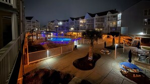 A nighttime view of a hotel courtyard with a swimming pool, palm trees, and outdoor seating areas. - Seascape 2202 The Seashell Pearl Beachfront Condo Gulf View Pool Hottubs Netflix (Galveston)