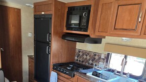 A compact RV kitchen with wooden cabinets, a black refrigerator, a microwave, and a stove. - Private space in a quiet area, great place to disconnect. (East Wenatchee)