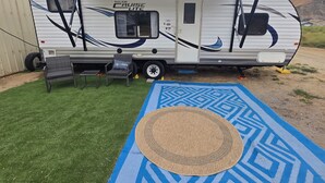A recreational vehicle with a covered living area, a small seating arrangement, and a patterned mat on the ground. - Private space in a quiet area, great place to disconnect. (East Wenatchee)