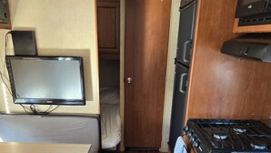 A compact RV kitchen with a stove, microwave, and a TV mounted on the wall. - Private space in a quiet area, great place to disconnect. (East Wenatchee)