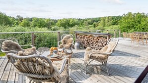 Terraza de madera con mobiliario de mimbre y una mesa lista para comer, con vistas a un área boscosa.