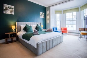 Een moderne slaapkamer met een groot bed, een nachtkastje, een stoel en uitzicht op gebouwen door grote ramen.