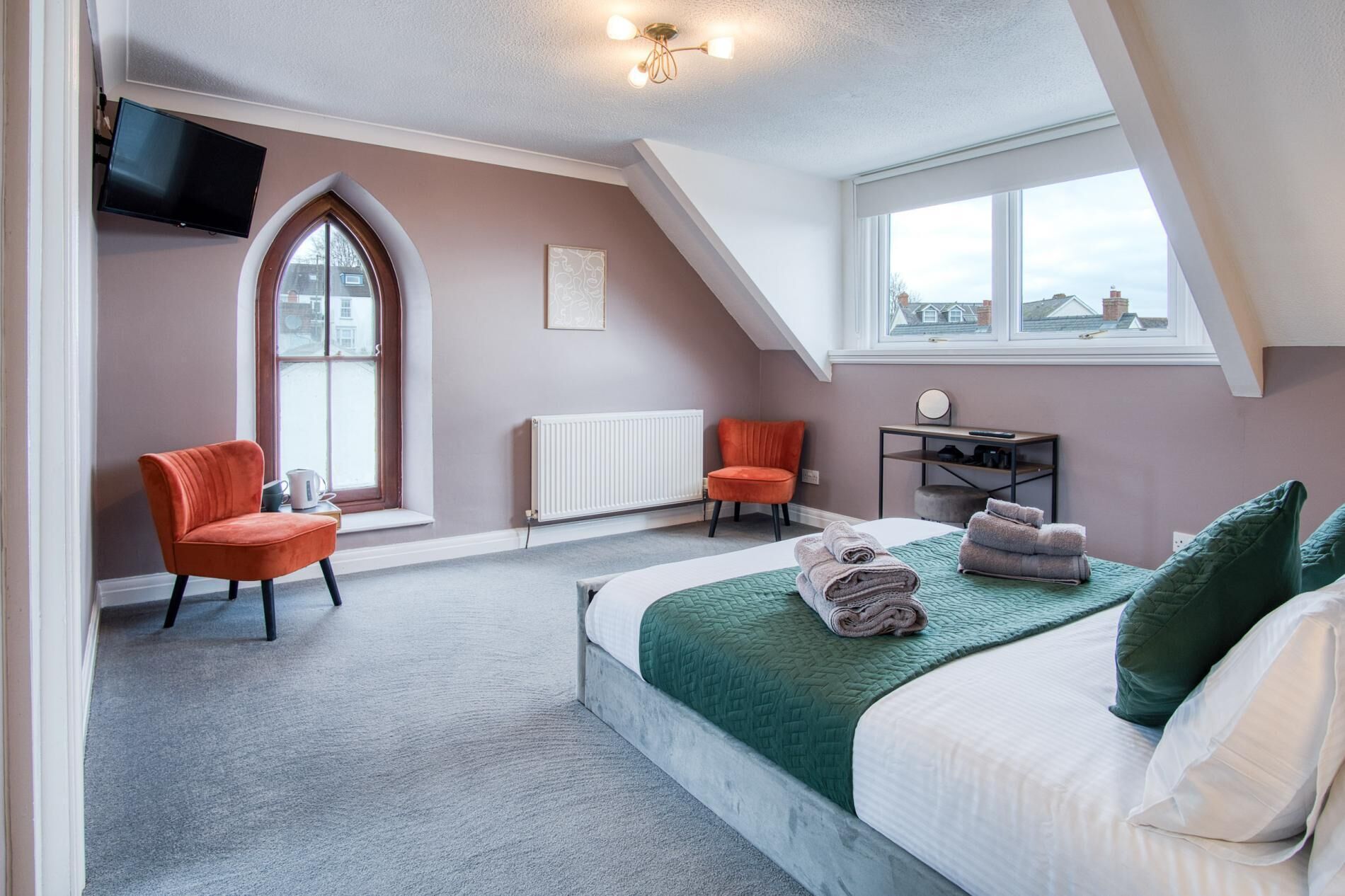 Une chambre à coucher comprenant un lit, deux chaises, un bureau, un radiateur et un téléviseur fixé au mur.