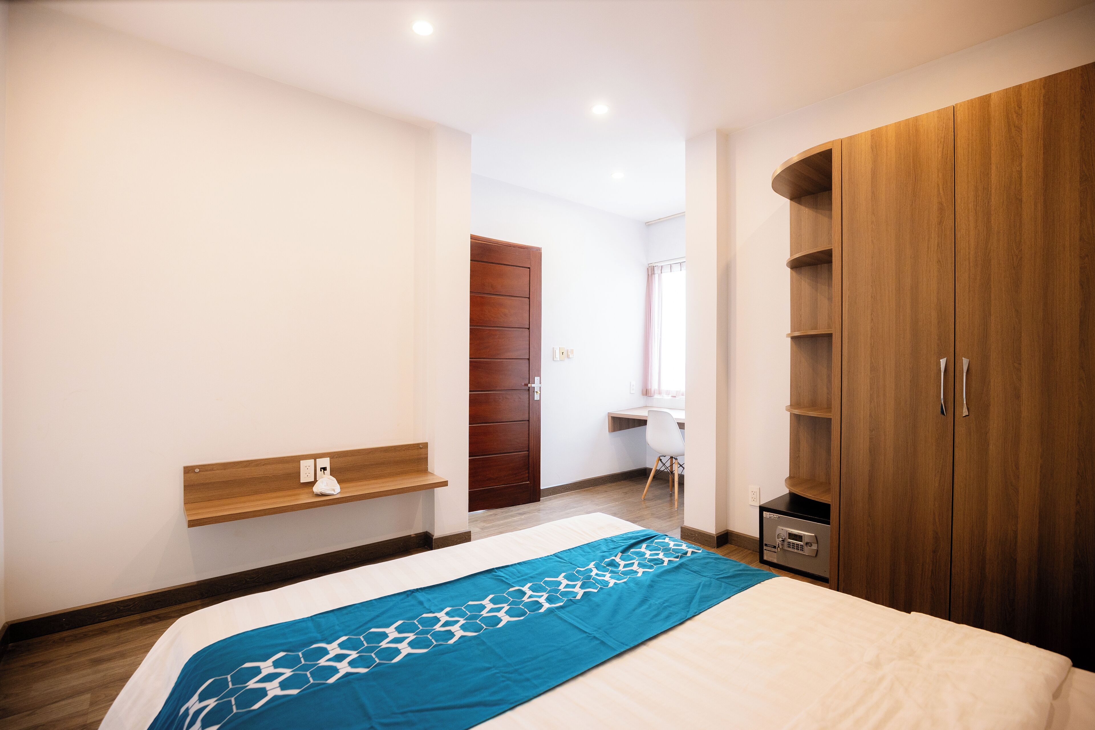 A bedroom with a bed, wooden wardrobe, bedside table, and a desk with a chair.