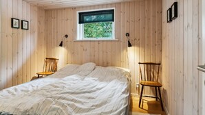 Un dormitorio con cama, dos sillas, una ventana con persianas y paredes de madera.