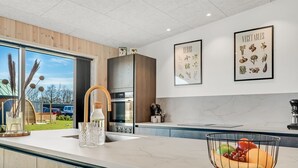 Une cuisine moderne dotée d’un grand îlot central, d’appareils électroménagers en acier inoxydable et offrant une vue sur l’extérieur.
