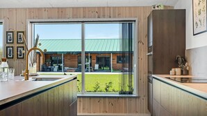 Une cuisine moderne avec des meubles en bois, une grande fenêtre et une vue sur un immeuble doté d’un toit végétalisé.