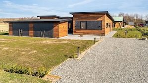Une maison moderne à deux étages, dotée d’un garage, d’un patio couvert et d’une allée gravillonnée.