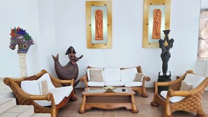 Una sala de estar acogedora con mobiliario de mimbre, una estatua de sirena y dos obras de arte enmarcadas en la pared.