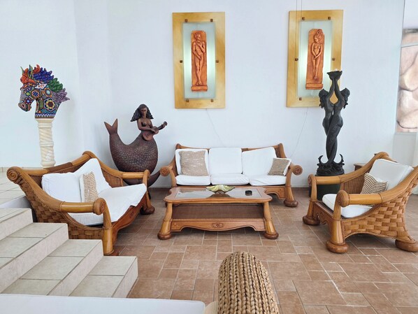 A cozy living area with wicker furniture, a statue of a mermaid, and two framed artworks on the wall. - Spacious hillside Villa with stunning bay&city views in Amapas, Puerto Vallarta (Puerto Vallarta)