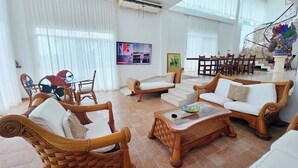A spacious living room with wicker furniture, a glass coffee table, and a dining area with wooden chairs and a table. - Spacious hillside Villa with stunning bay&city views in Amapas, Puerto Vallarta (Puerto Vallarta)