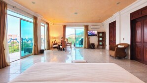 Amplia habitación de hotel con una cama grande, un comedor, televisión y vistas al exterior.