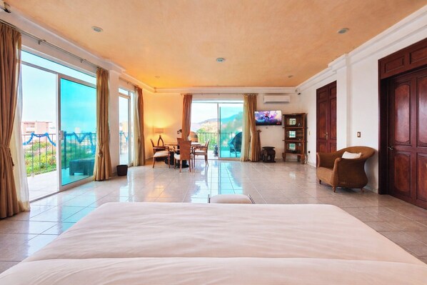 A spacious hotel room with a large bed, a dining area, a TV, and a view of the outdoors. - Spacious hillside Villa with stunning bay&city views in Amapas, Puerto Vallarta (Puerto Vallarta)