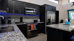 A modern kitchen with dark cabinets, a granite countertop, a built-in microwave, a stainless steel refrigerator, and a coffee maker.